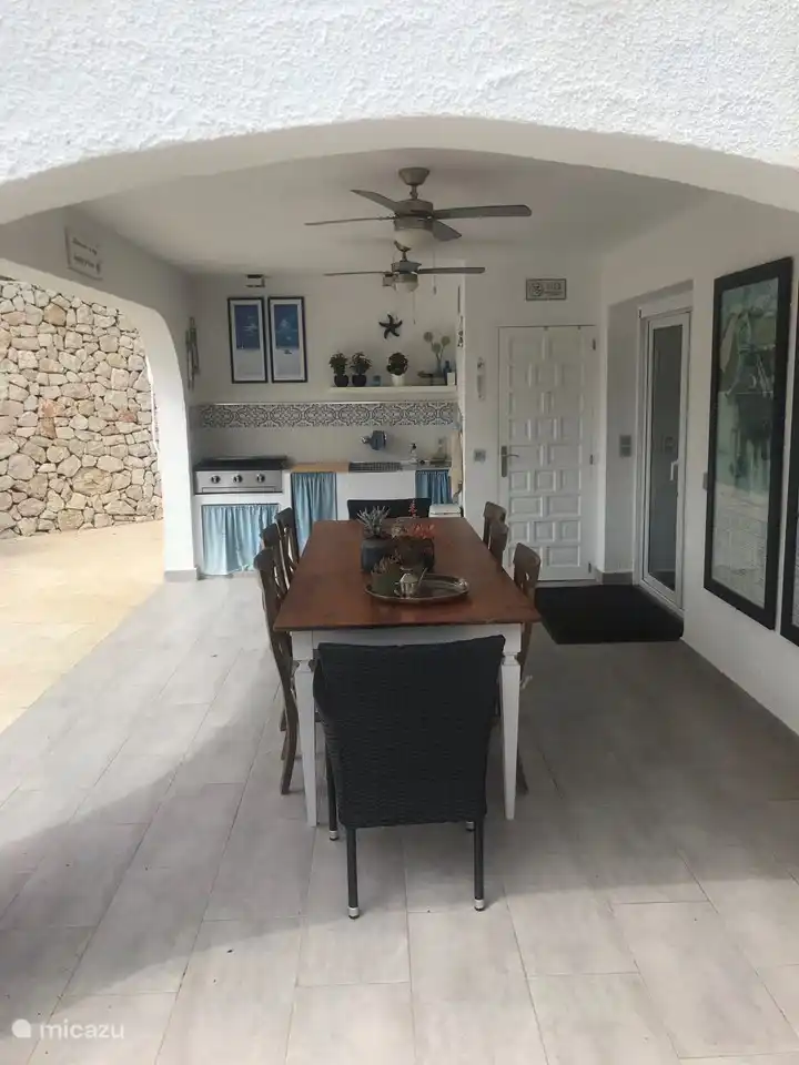 Het overdekte terras aan de zijkant van de villa.
Op de achtergrond de buitenkeuken. Links is het zwembad en rechts de openslaande deuren naar de woonkamer van de beneden verdieping.