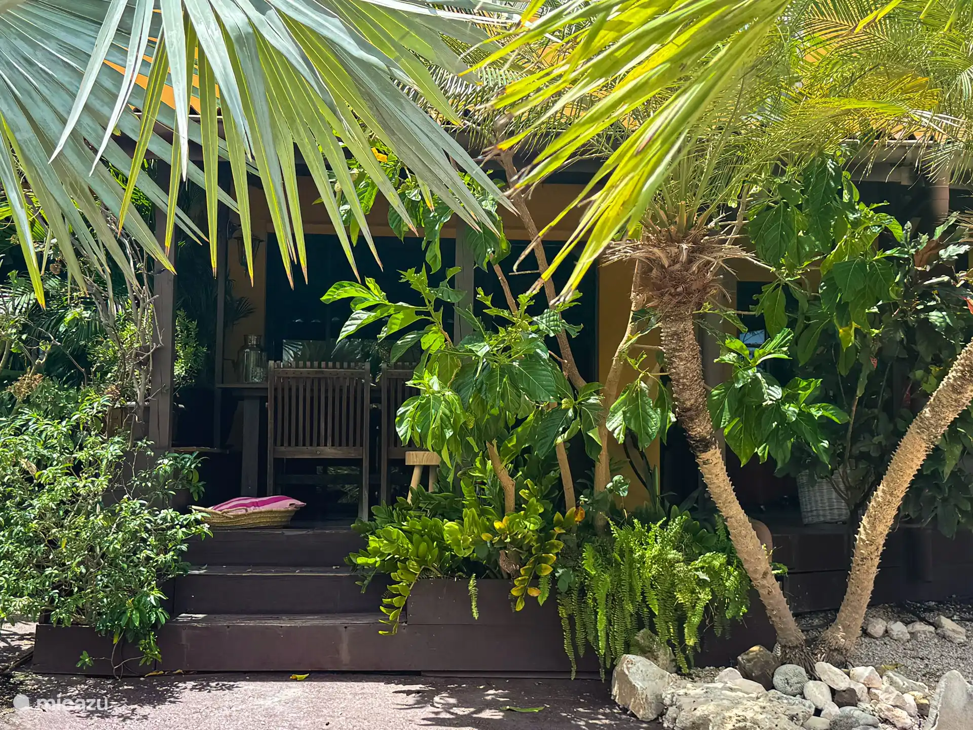 La terraza, rodeada de palmeras y jazmines, ofrece un sofá, una tumbona, una mesa de comedor y una barbacoa.
