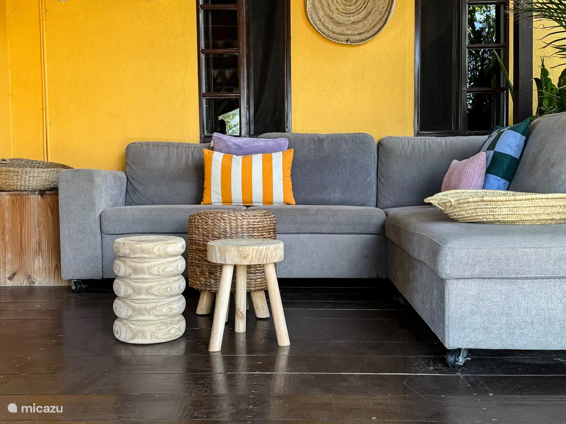 La amplia y sombreada terraza está rodeada de palmeras y flores. En la terraza hay un cómodo sofá salón, un sofá salón, una mesa de comedor de madera, sillas y barbacoa.