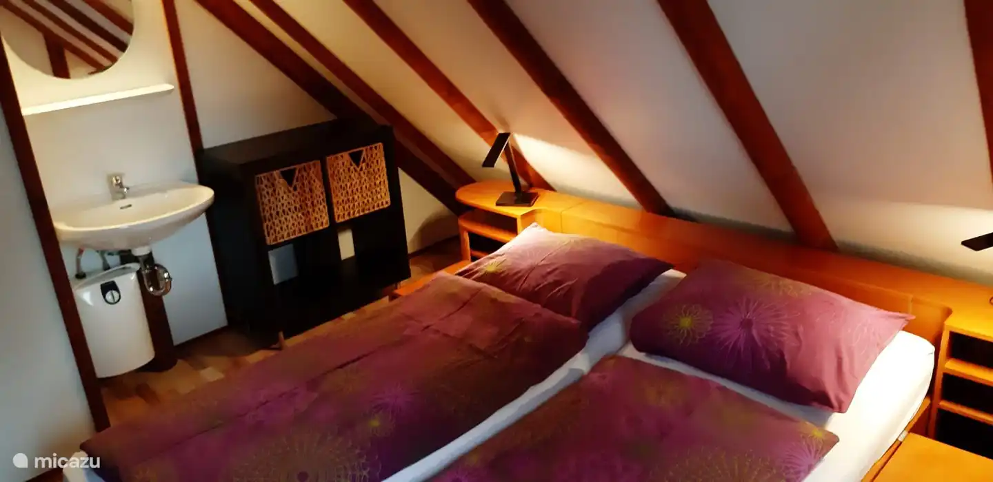 Schlafzimmer 2: im Obergeschoss mit bequemem Auping-Bett 160 x 200 cm. Zugang zum Balkon und Verdunkelungsrollläden. Die Nachttischlampen verfügen über einen USB-Anschluss für Ihr Mobiltelefon. Waschbecken.