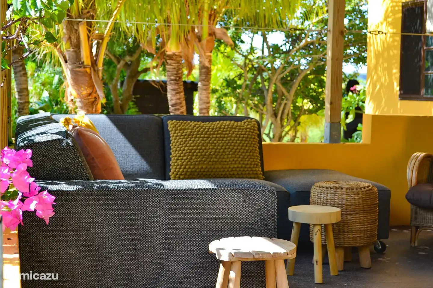 El apartamento con la terraza a la sombra en el jardín tropical. La terraza ofrece un sofá lounge, un sofá lounge, una gran mesa de comedor, barbacoa y una hermosa vista de las colinas de Curazao.