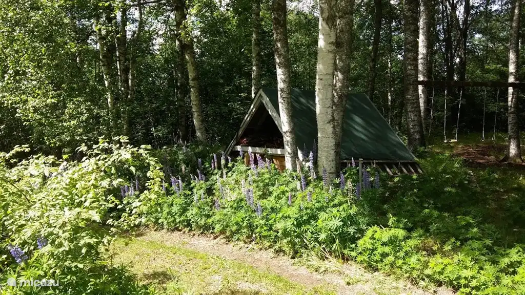 Holzhaus und die beiden Schaukeln mit der Feuerstelle dahinter.