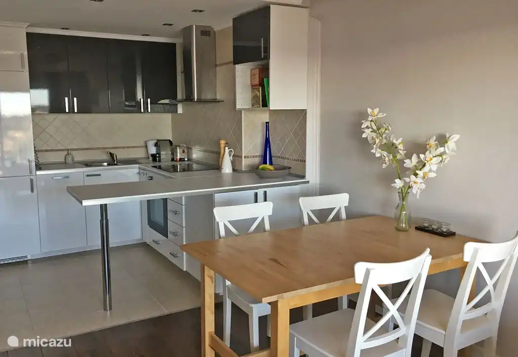 Wohnzimmer mit Esstisch und offener Küche mit Geschirrspüler, Kühlschrank, Gefrierschrank, Herd, Ofen und Nespresso-Kaffeemaschine.