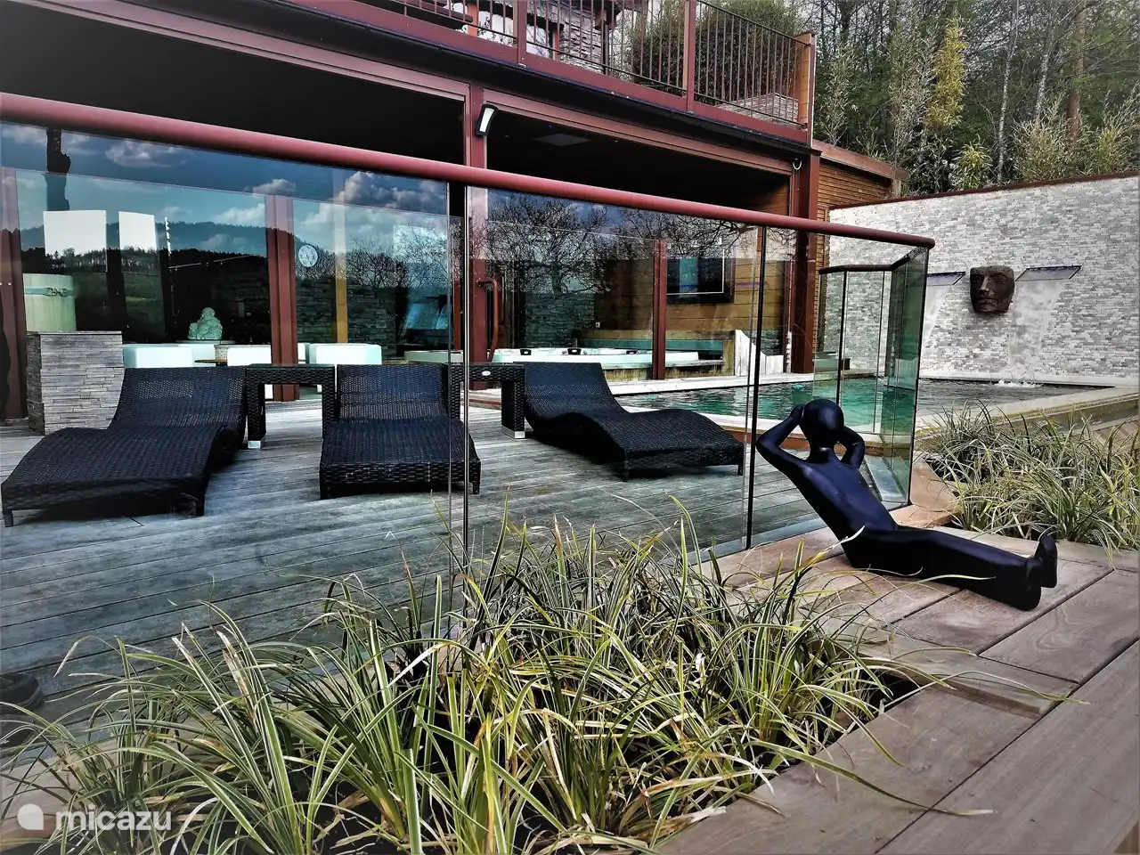 Das Schwimmbad, die großen Sonnenliegen und der dahinter liegende Indoor-Wellnessbereich.