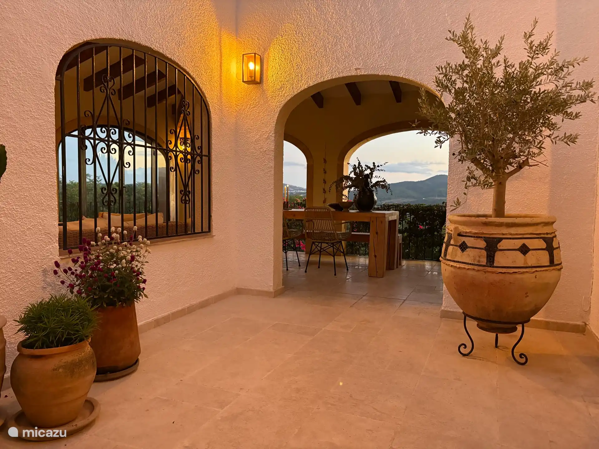 En 2026 rediseñamos el patio, con varias plantas sobre y alrededor de una mesa de mosaico y una maceta grande con nuestro propio olivo. La iluminación también es nueva.