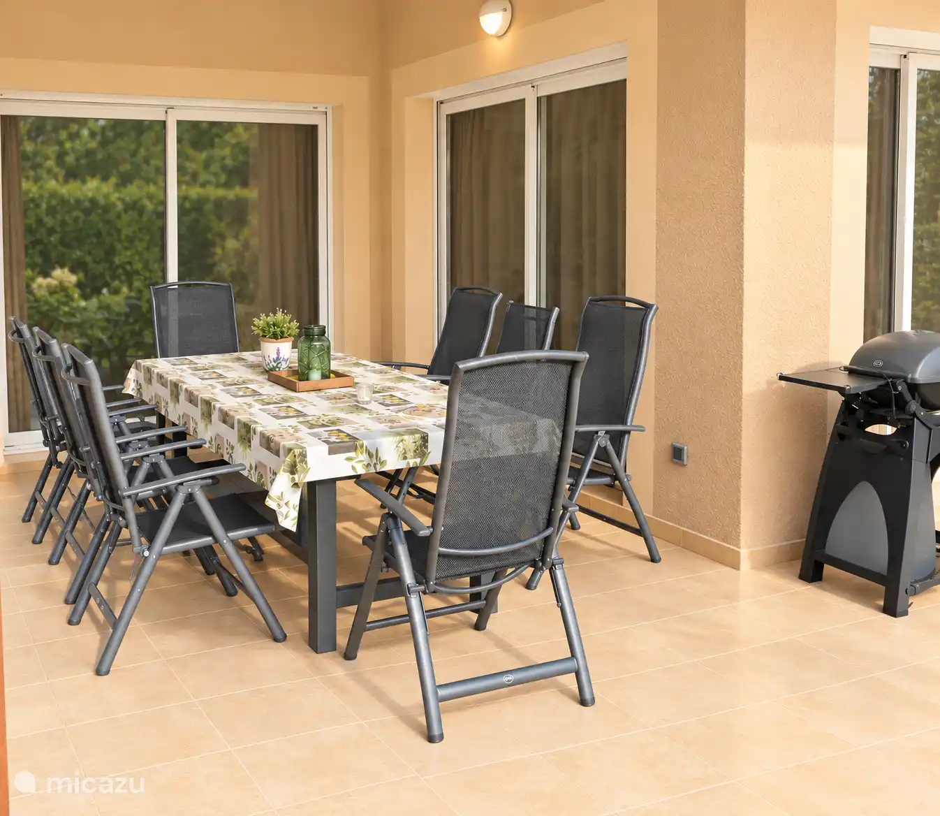 Terras onder de veranda met grote eettafel, verstelbare stoelen en elektrische Weber BBQ