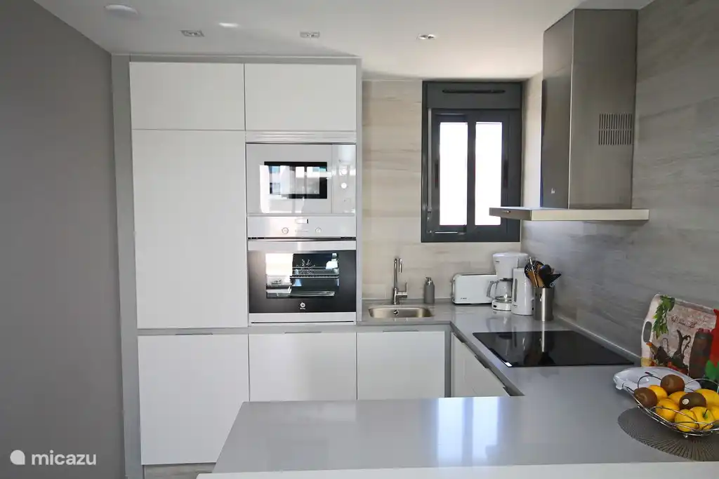 Compleet ingerichte keuken met vaatwasmachine, koel-vriescombinatie, magnetron, oven, kookplaat en afzuigkap.