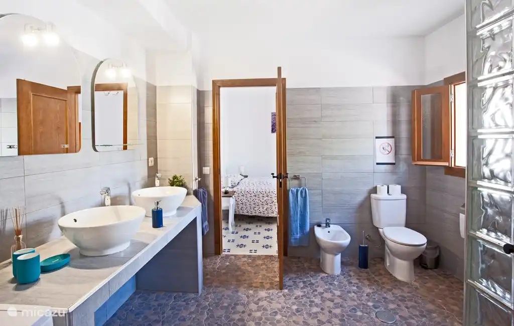 De blauw/grijze grote badkamer aan de voorkant van het huis met de grote inloopdouche en wasmachine.