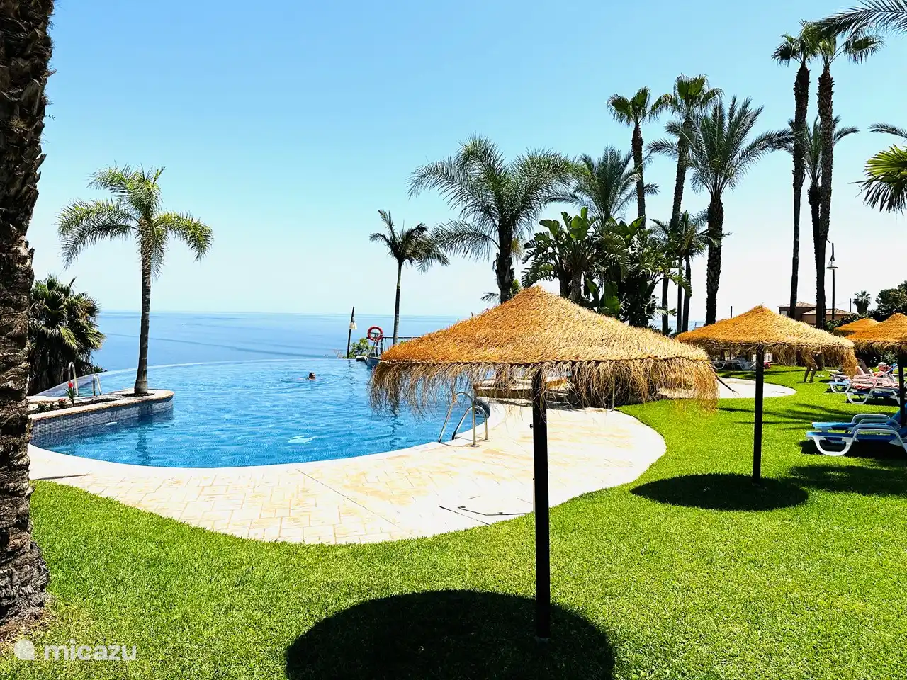 Liegen unter Palmen und Sonnenschirme am Infinity-Pool