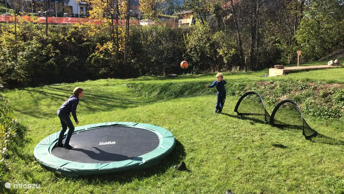 Vue de la terrasse sur le jardin. Profitez du trampoline, jouez au football, au badminton ou détendez-vous au soleil. Il y a une cabane forestière au fond du jardin. Celui-ci est accessible par une passerelle au-dessus du ruisseau. Vous pouvez construire de beaux barrages dans le ruisseau !