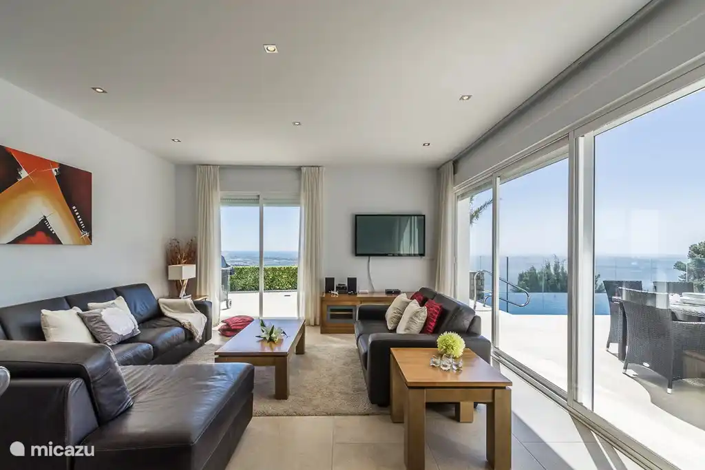 De woonkamer heeft een grote schuifpui naar het terras en uitzicht over zee