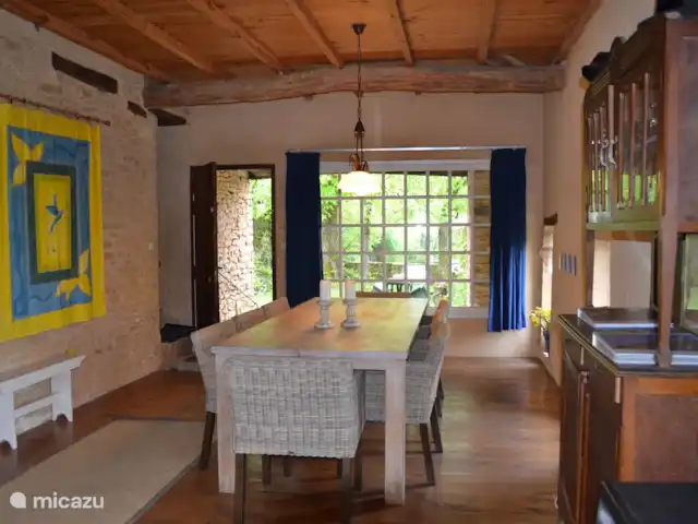 Chez Nous en Francia, Dordoña, Le Buisson-de-Cadouin - casa de campo La parte de la sala de estar con mesa de comedor larga de madera, espacio suficiente para 8 personas. Sillas fáciles y robustas con reposabrazos y cojín. La ventana con las cortinas azules da a la terraza lateral y a la zona verde hacia la piscina. A esta terraza se puede llegar a través de la puerta y la escalera de piedra.