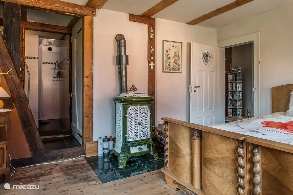 Großes Schlafzimmer für 2 Personen mit Holzofen und Blick auf die Dusche. Die Wände dieses Raumes sind ebenfalls mit Lehm verkleidet. Um die Betten herum befinden sich Moskitonetze, damit Sie ruhig schlafen können, ohne dass Mücken summen.