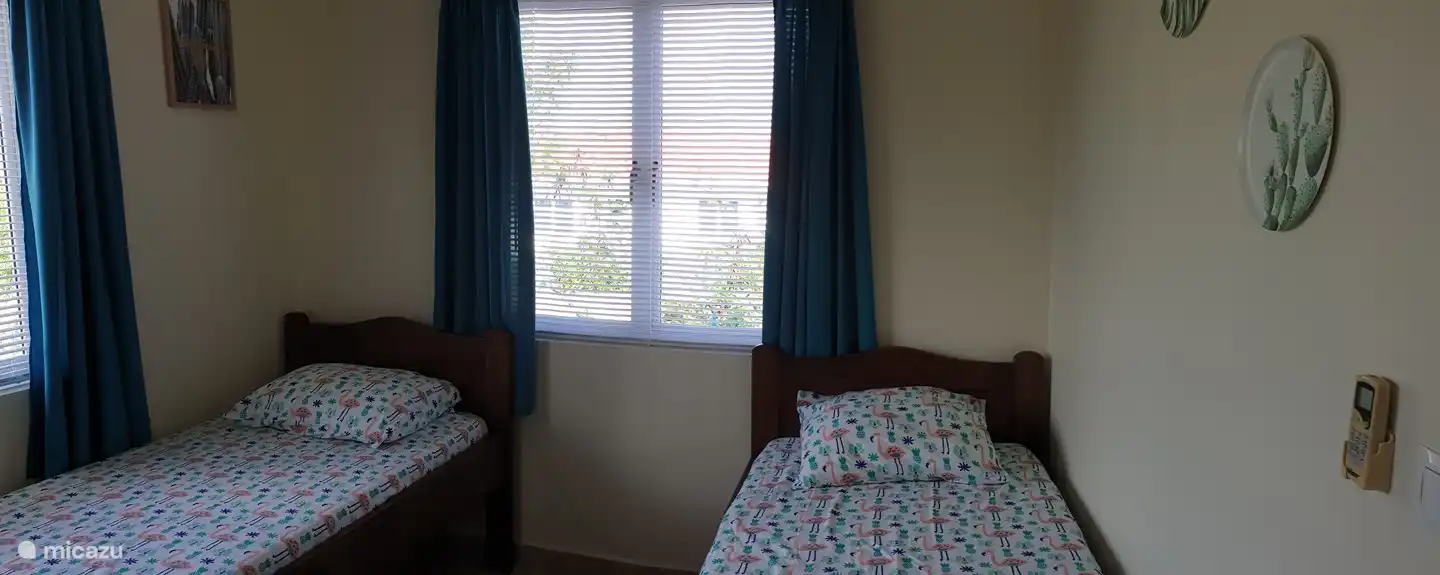 Schlafzimmer mit 2 Einzelbetten. Luxaflex und Vorhänge vor den Fenstern. Klimaanlage