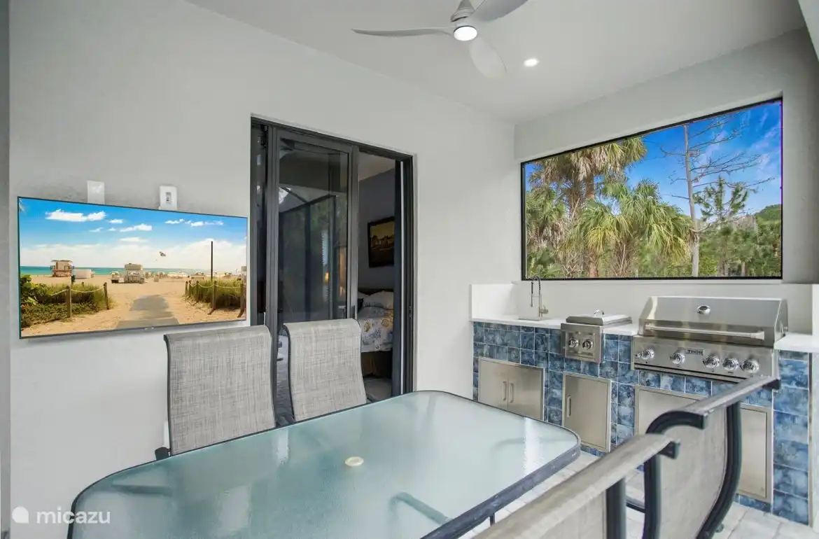 Esstisch im Freien, TV, Außenküche mit 2 Gaskochfeldern, eingebaute Grillspüle. Rechts ist die Aussicht und links der Fernseher