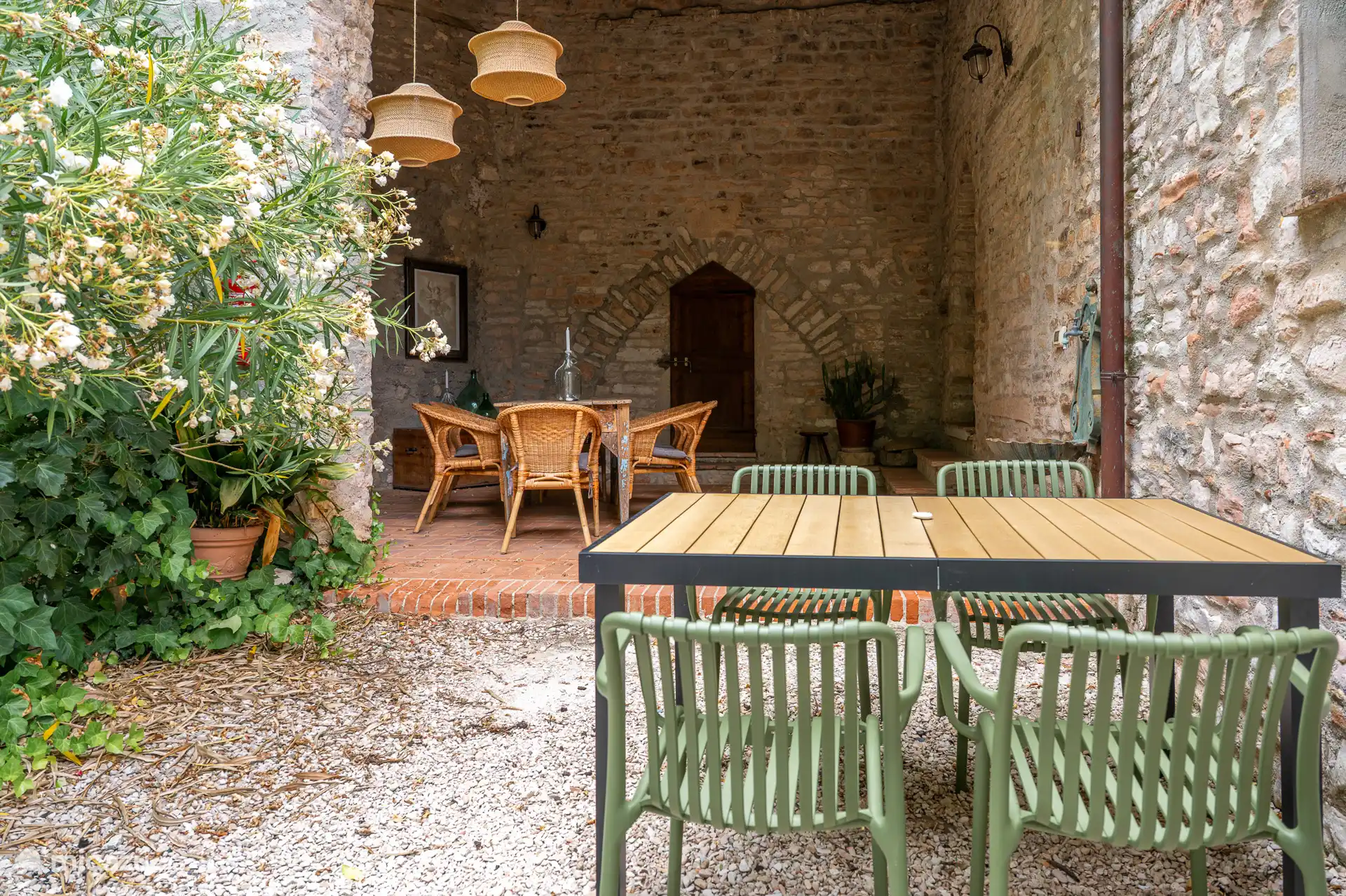 Buitenterras met eettafel, omringd door authentieke stenen muren en bloeiende planten. 