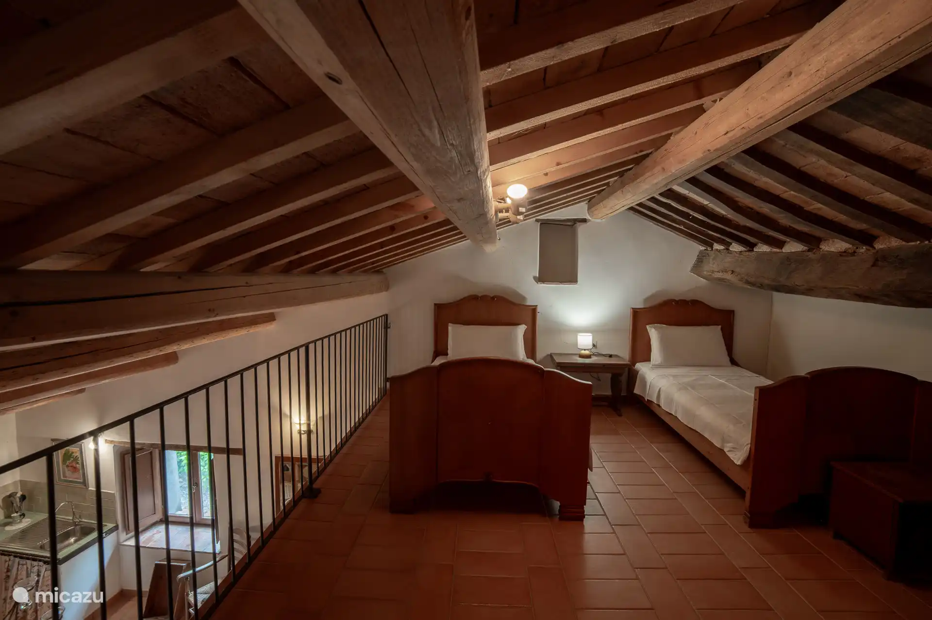 Rustige slaapkamer met twee eenpersoonsbedden, ingericht onder het originele balkenplafond.