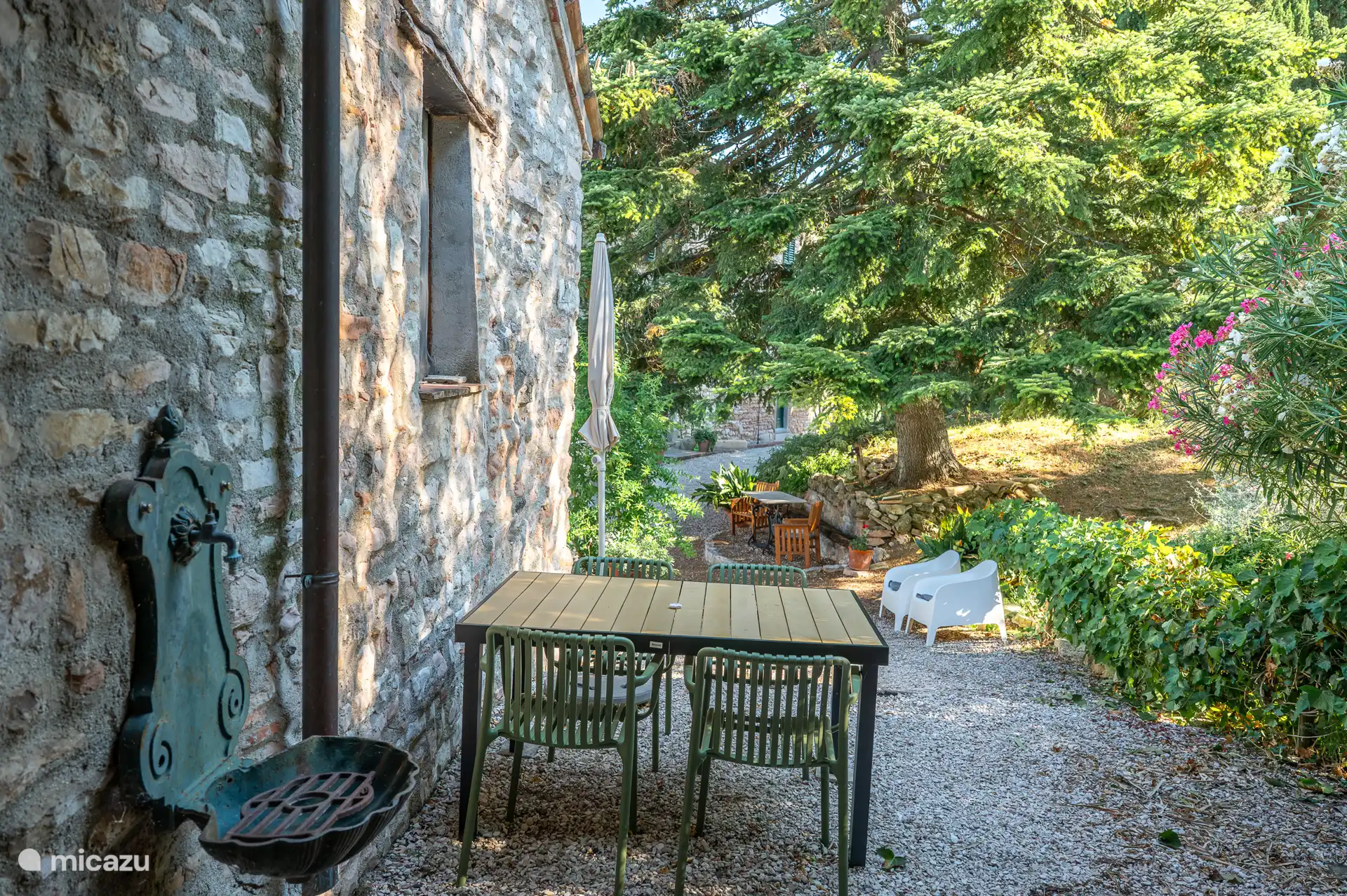 Buitenzicht op de karakteristieke stenen gevel, met eettafel in de tuin omringd door groen. 