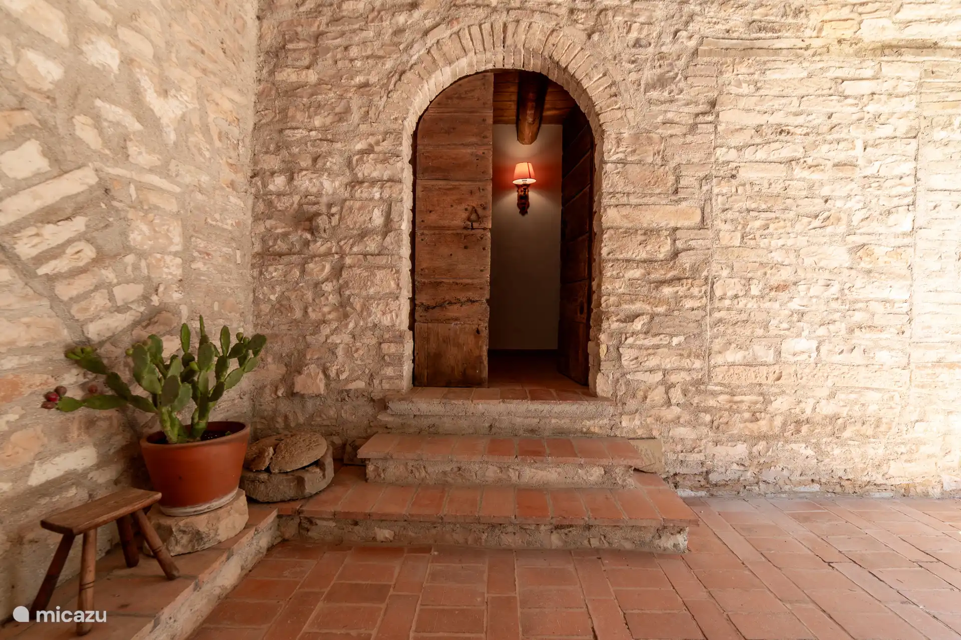 Authentieke stenen entree met traditionele boogdeur en terracotta trapje.