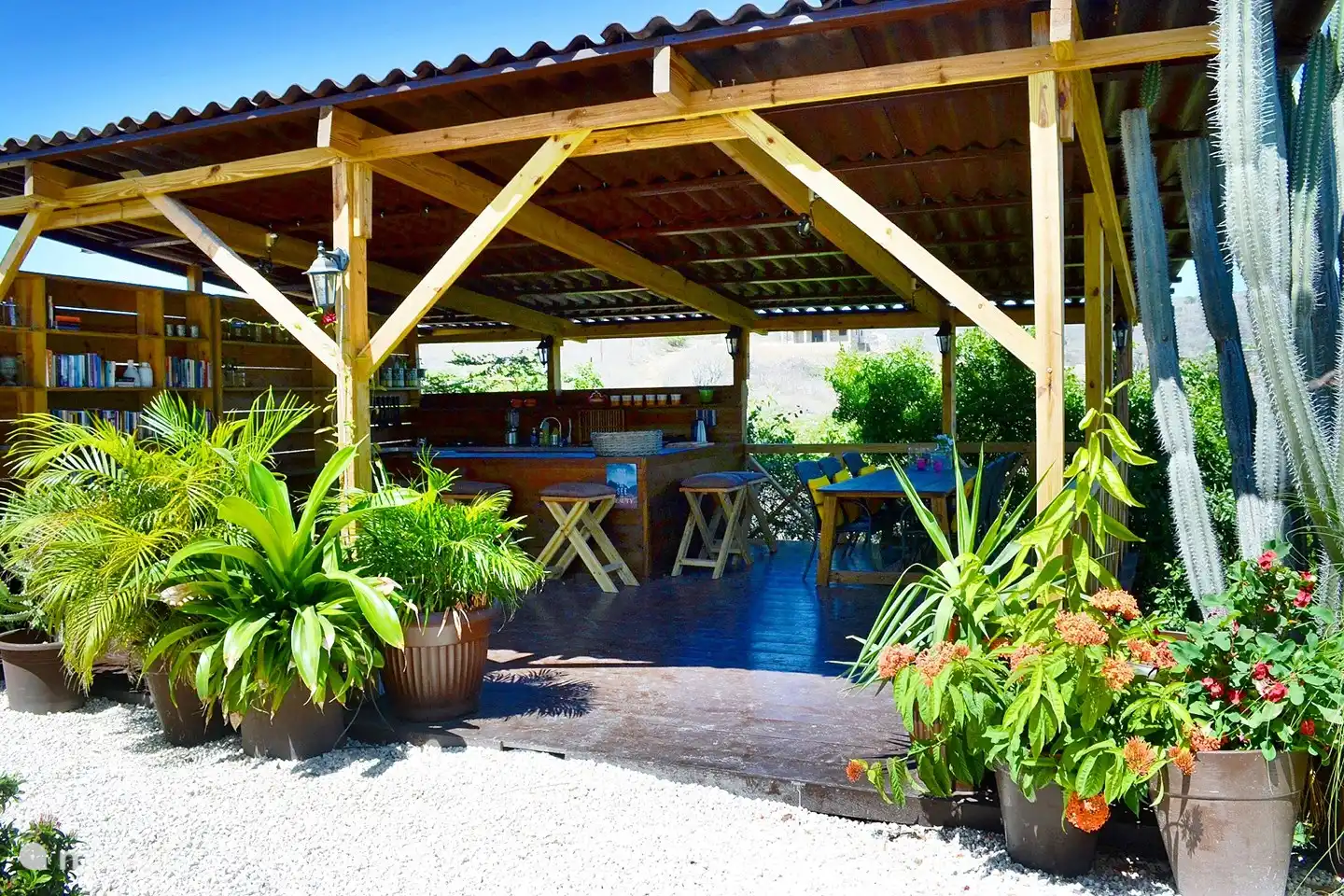 La cocina exterior, cerca del estudio, con mesa de comedor a la sombra y una pequeña biblioteca.