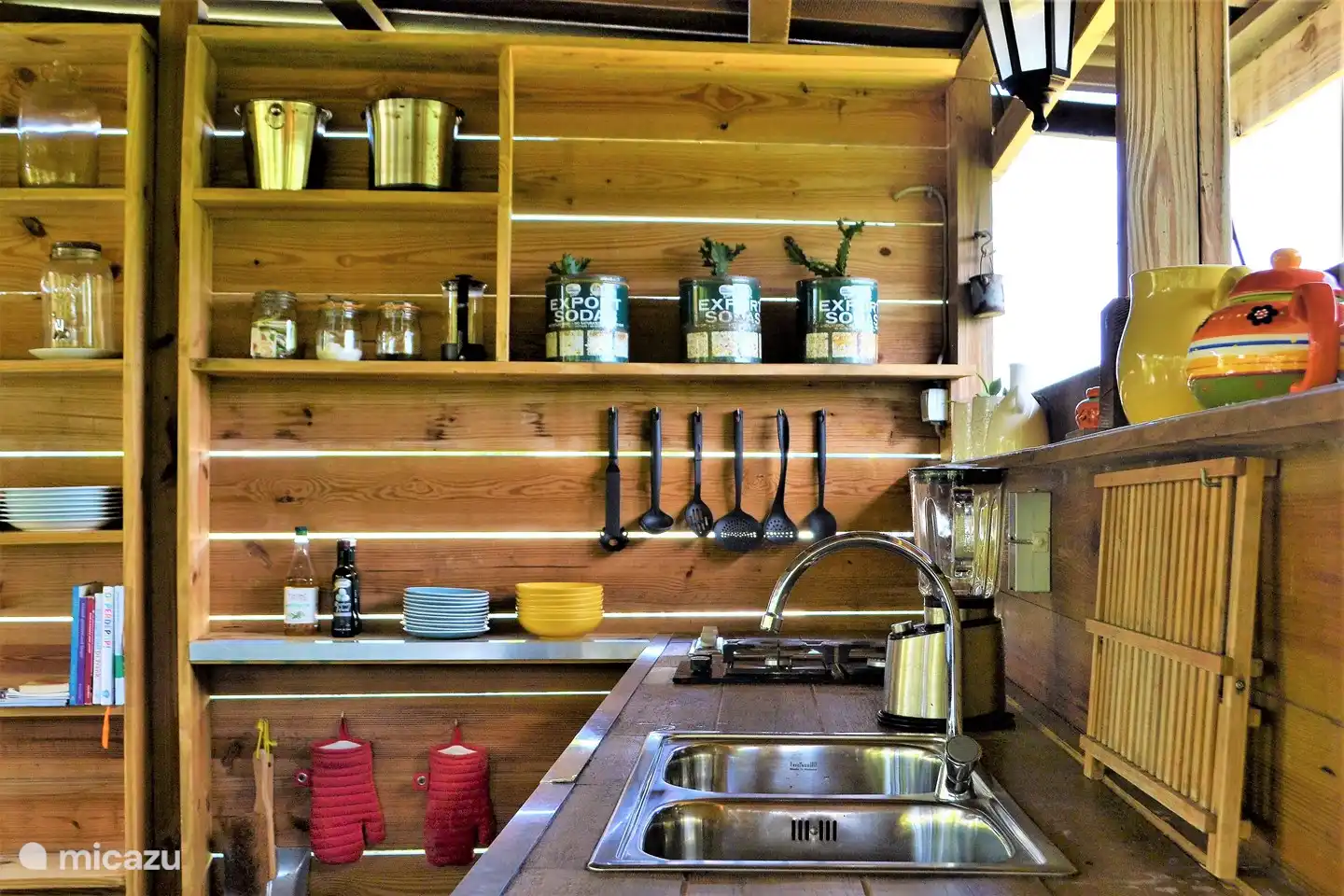 La cocina exterior, cerca del estudio, con mesa de comedor a la sombra y una pequeña biblioteca.