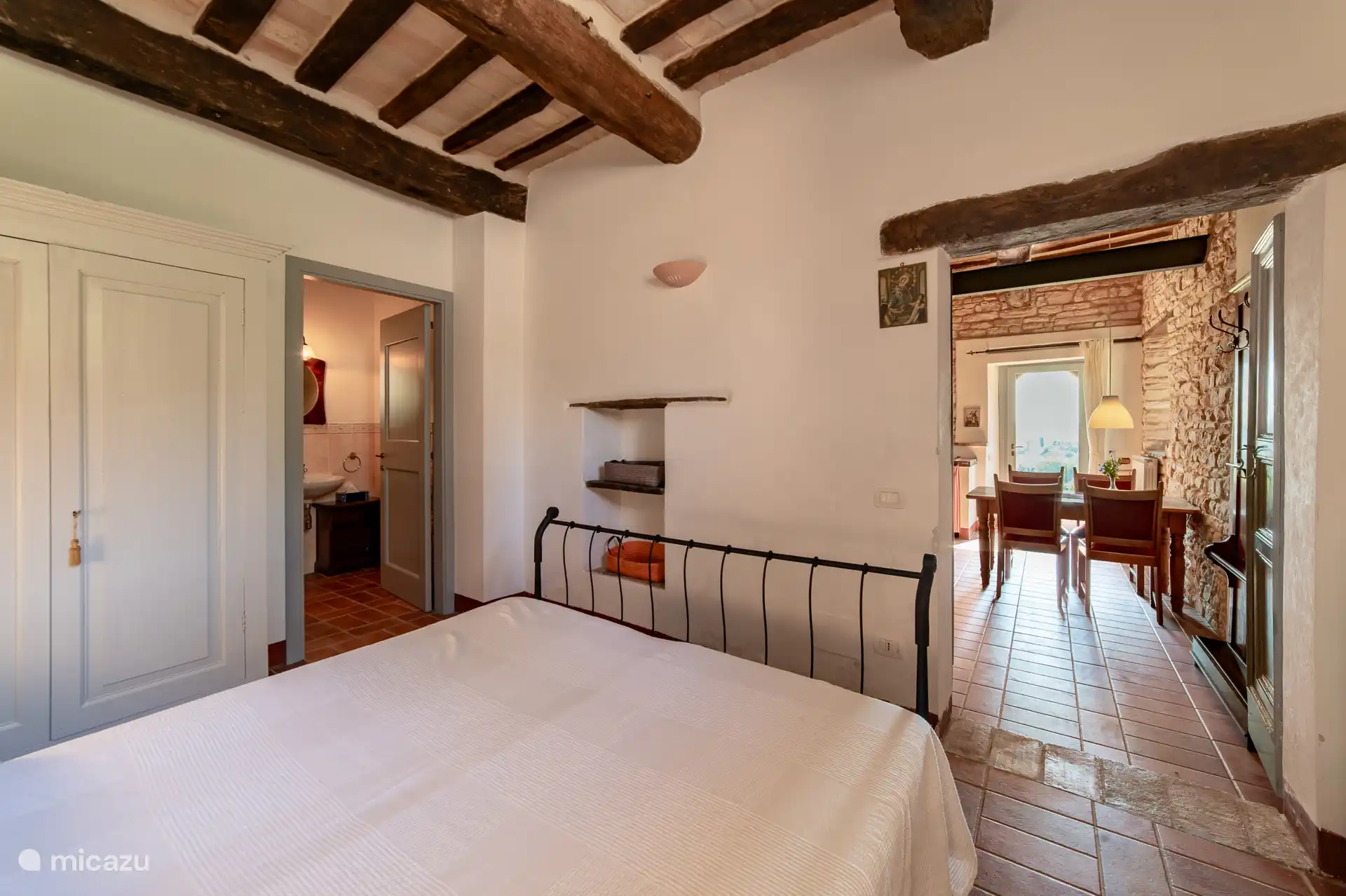 De slaapkamer van Melograno met doorkijk naar de woonkamer en badkamer. Een ruimte vol authentiek Italiaans karakter, met originele houten balken en warme sfeerverlichting.