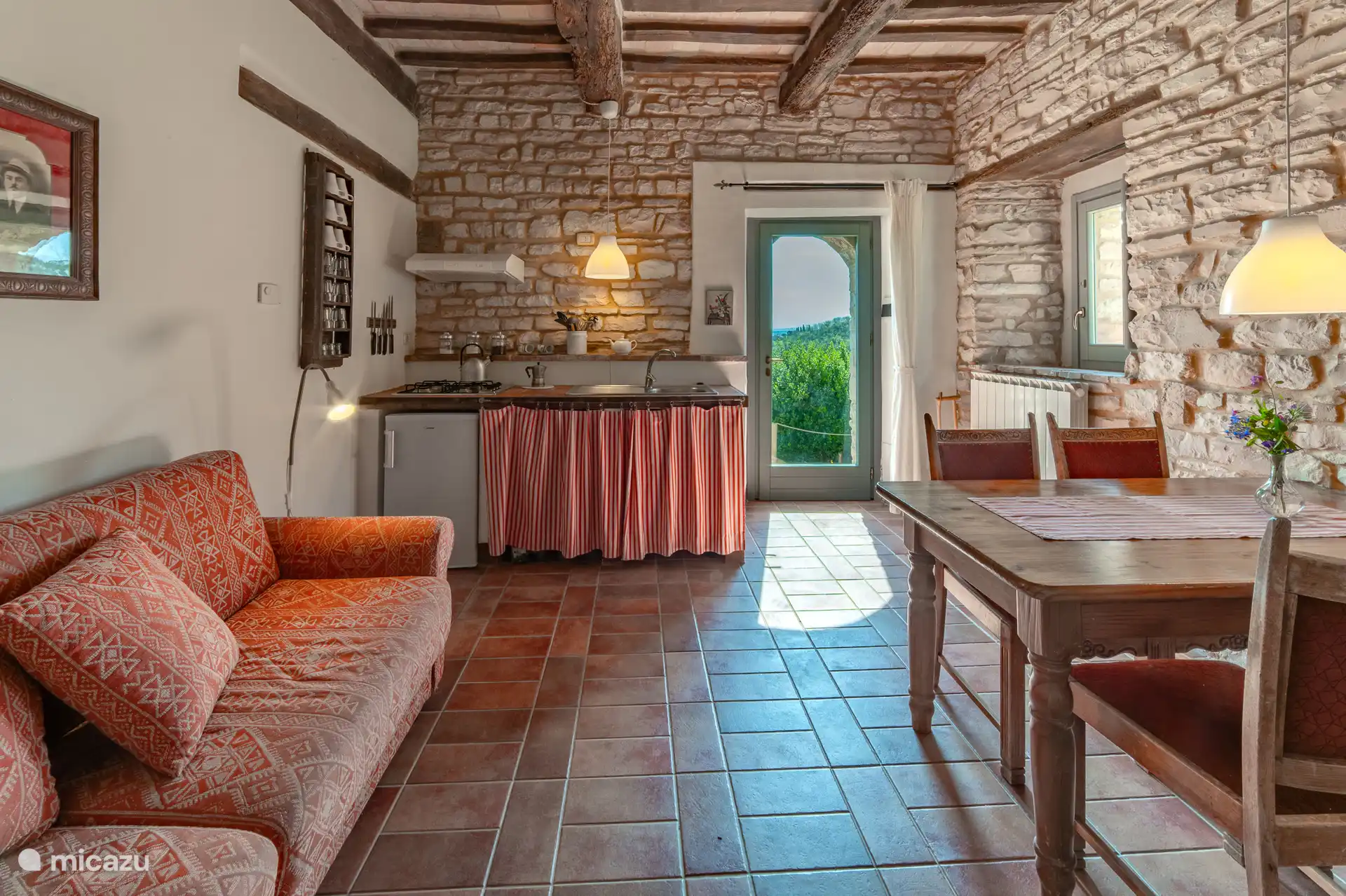 De gezellig woonkamer van Melograno met zithoek, keuken en uitzicht over de heuvels van Le Marche. De comfortabele slaapbank biedt slaapplaats voor 2 extra personen. Ideaal voor een verblijf van 4. 