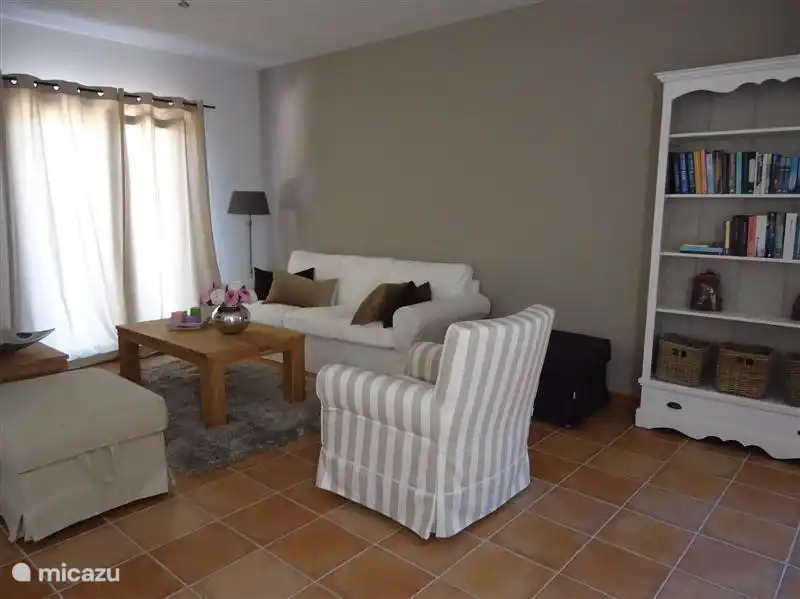 Coin salon avec canapé 3 places, fauteuil, TV et 2 poufs.