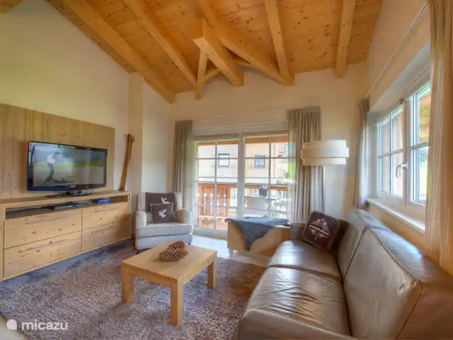 Resort de montaña Kaprun TopE20 en Austria, Salzburgo, Kaprun - apartamento Después de un exitoso día en las montañas, puede relajarse en el lujoso sofá de la sala de estar. Los techos altos con hermosas vigas contribuyen a crear un ambiente espacioso y relajante.