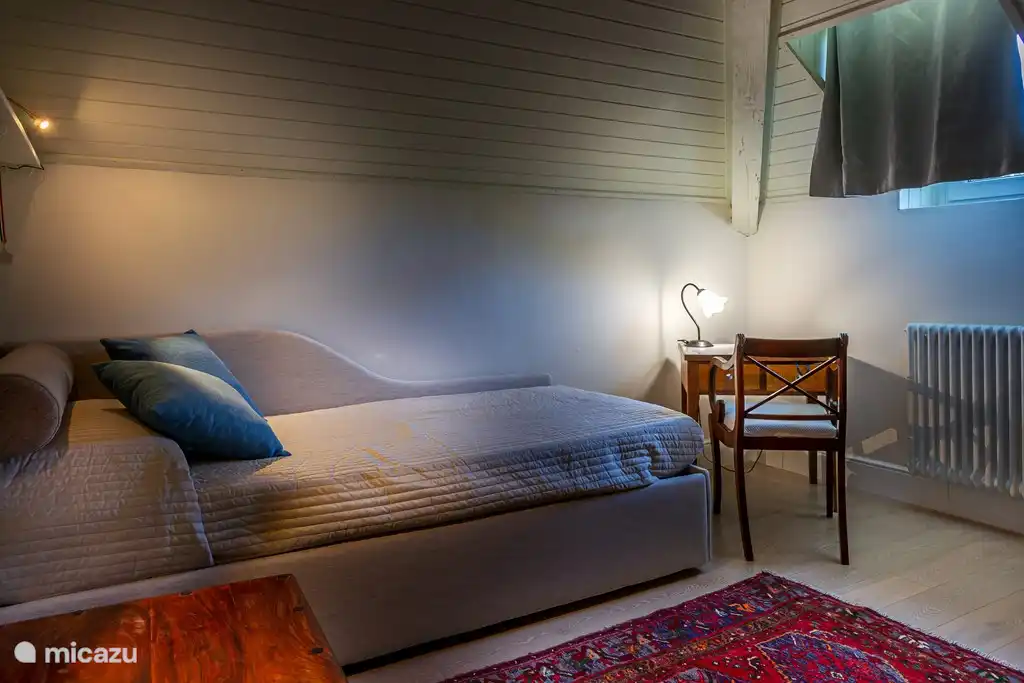 Dormitorio con una cama individual y mezcla de muebles antiguos y modernos. Ventana con vistas a la costa.