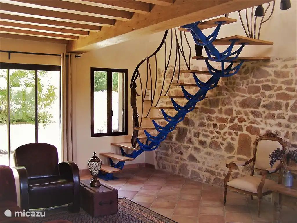 In dem großen Wohnzimmer mit authentischer en pierre Wand eine Eisentreppe, die von einem regionalen Künstler hergestellt und ausgeführt wurde. Durch die Terrassentüren gehen Sie in den Garten hinter dem Haus.