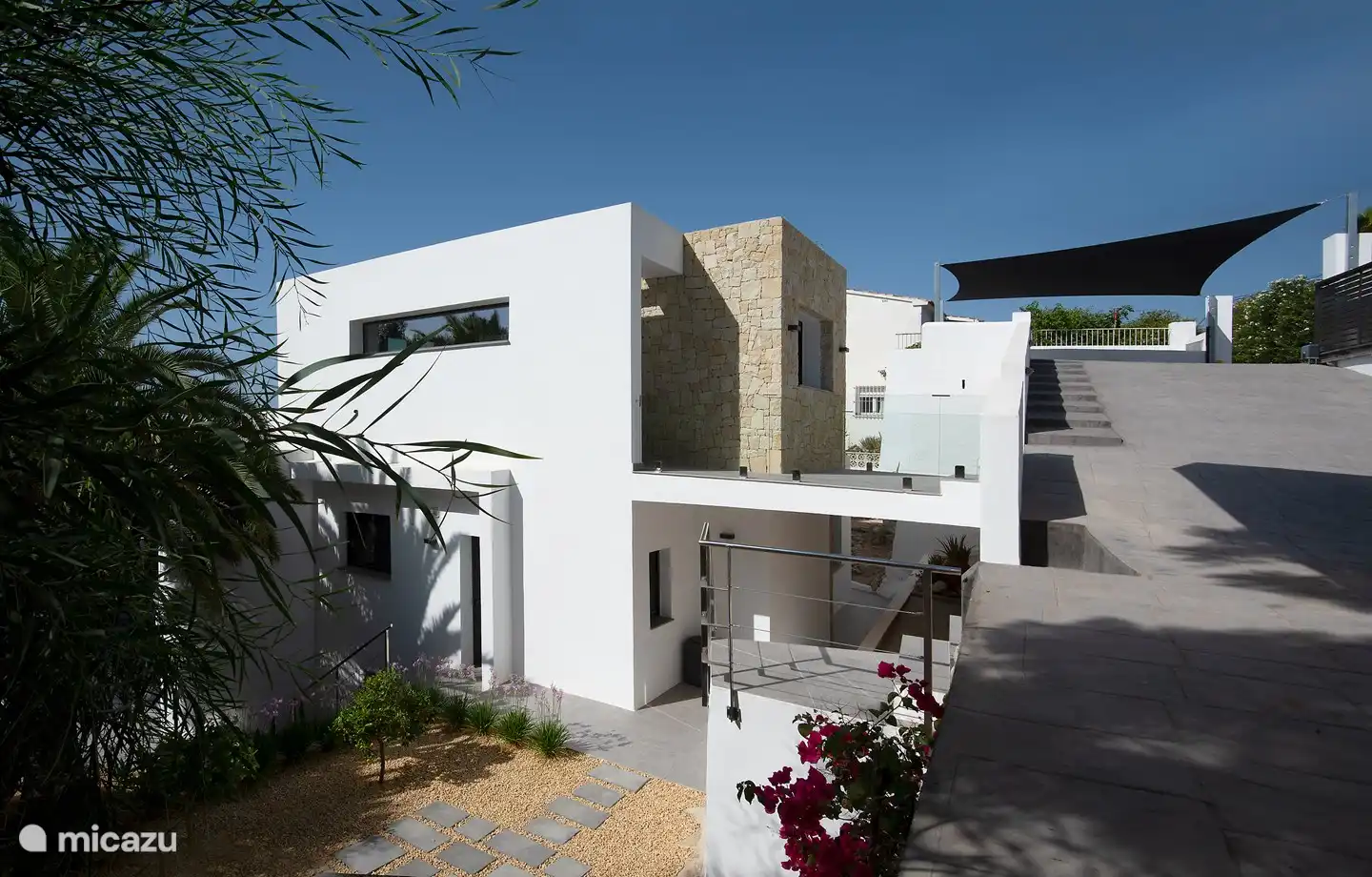 Am Ende der Auffahrt mit Blick auf das Haus und den überdachten Parkplatz. Die Autos stehen im Schatten.