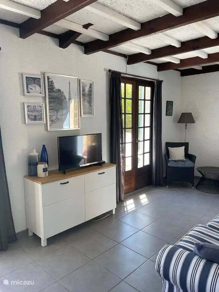 Wohnzimmer mit Fernseher, 2-Sitzer-Sofa, 2 Stühlen, Tisch und Bücherregal voller verschiedener Literatur.