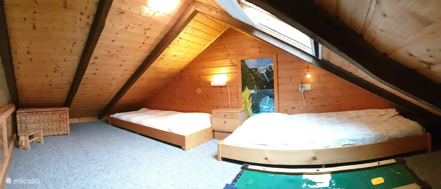 Foto panorámica de loft con camas separadas. Hay juguetes para niños en una cesta de mimbre.