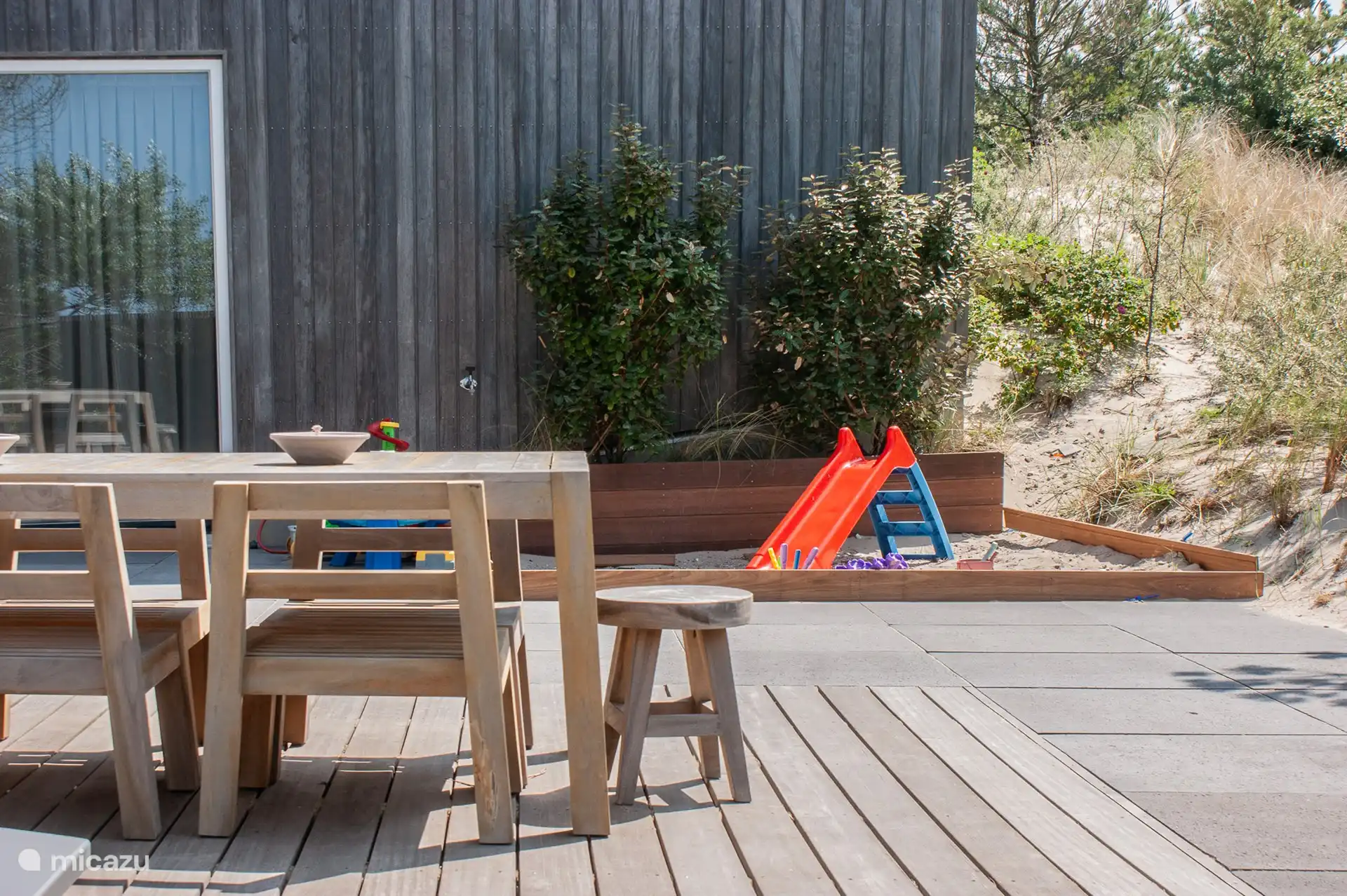 Terrace with large teak table, parasol, sandpit with slide and outdoor toys.