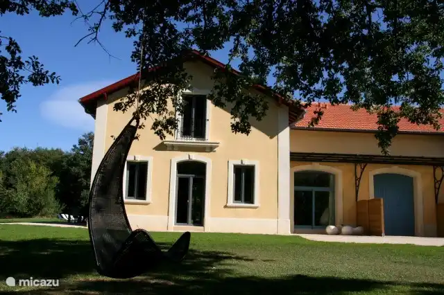 Voorzijde van de vakantiewoning met twee gezellige schommels die bevestigd zijn aan de oude eiken in de tuin