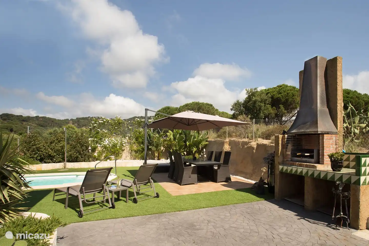 The large dining table with large umbrella next to the BBQ