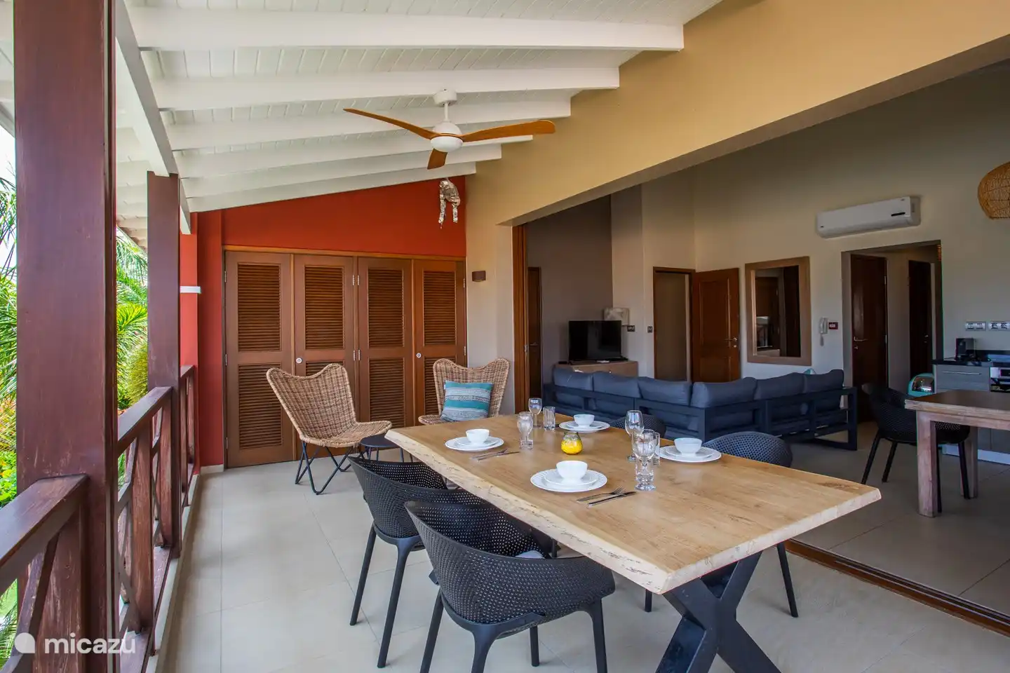 Schaduwrijk balkon met eettafel en open deuren naar binnengedeelte.