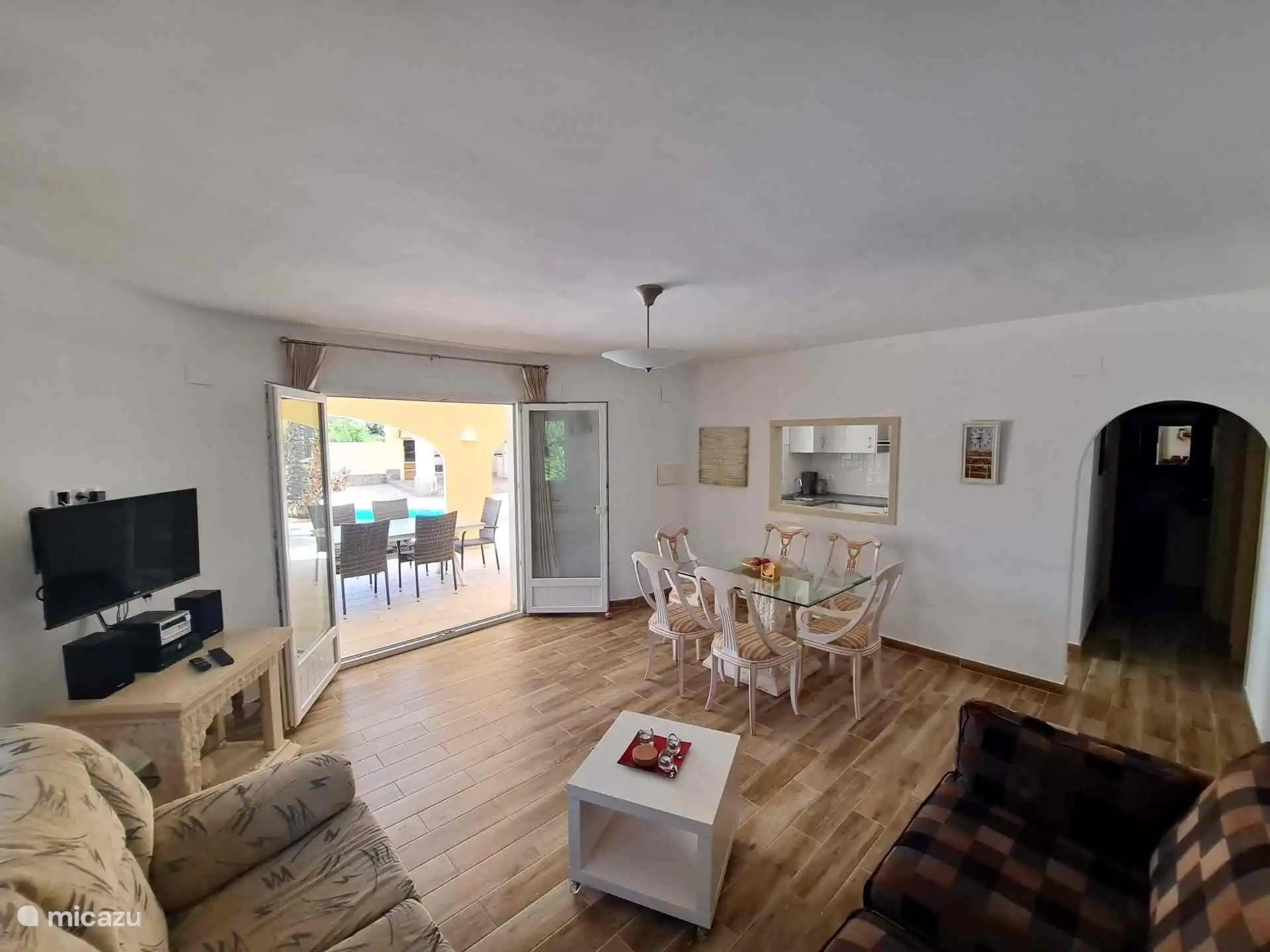 Salon begane grond, vanaf de andere kant gezien. Rechts de gang naar de slaapkamers en de badkamers en links het gezellige open raam van de keuken.