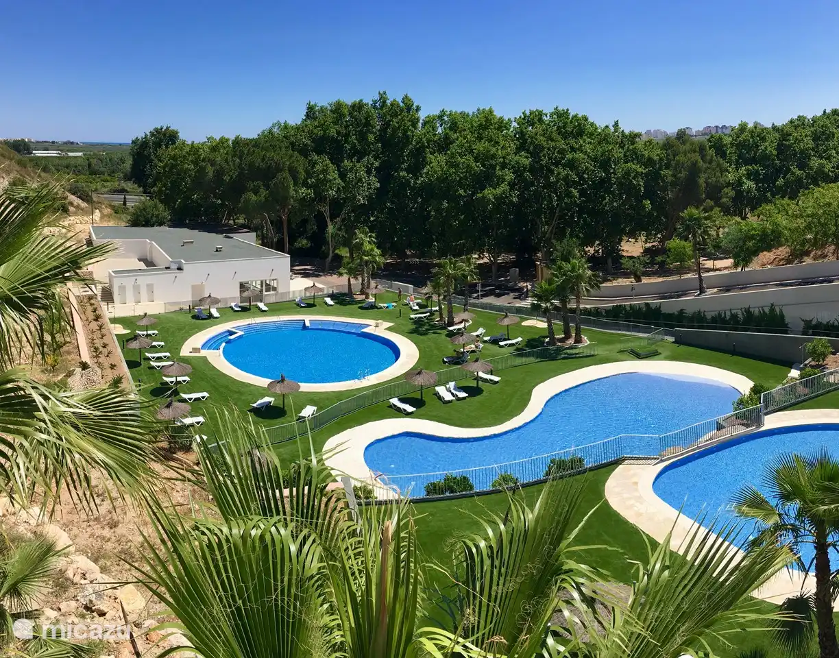 3 piscinas con tumbonas, sombrillas, duchas, aseos y sala de fitness en el edificio blanco