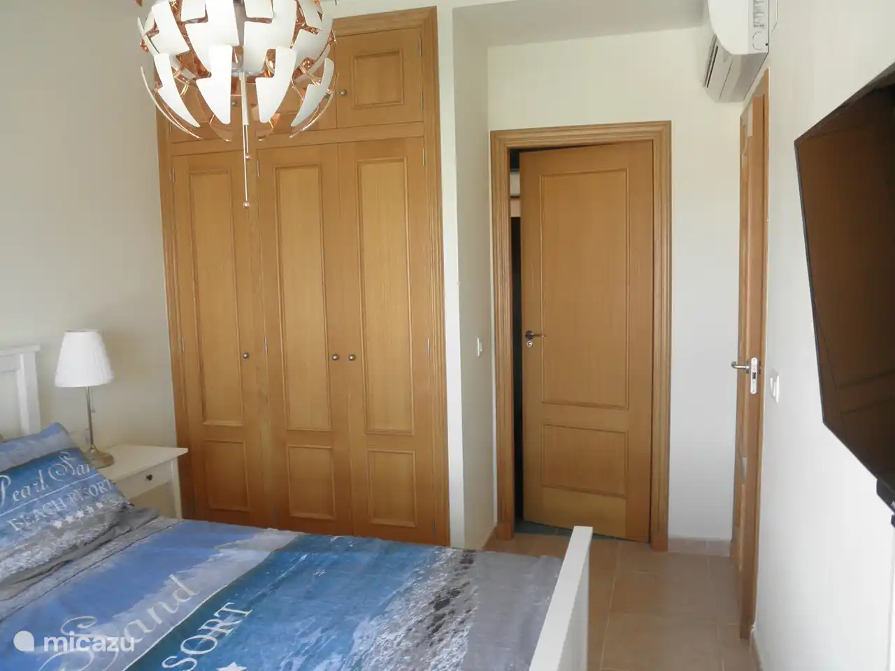 dormitorio principal con pantalla de TV y unidad de aire acondicionado y una vista de la puerta del baño privado.