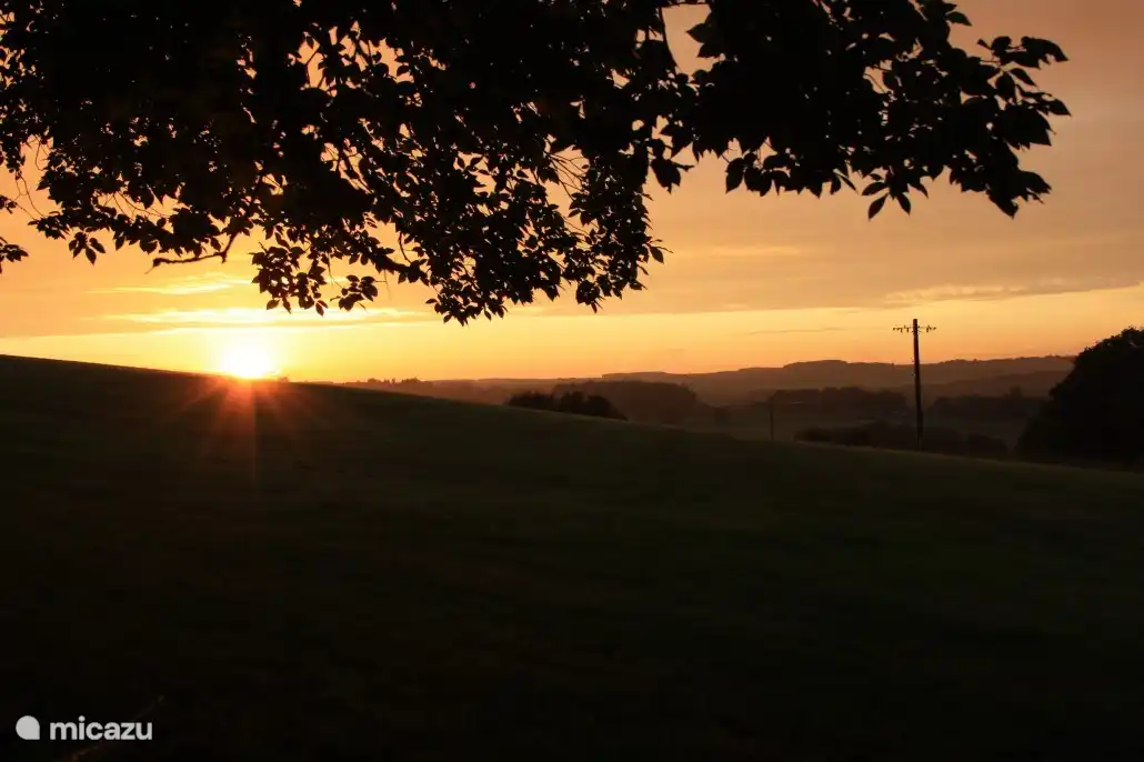die untergehende Sonne auf der Rückseite des Hauses, auf der sich eine Bank befindet.