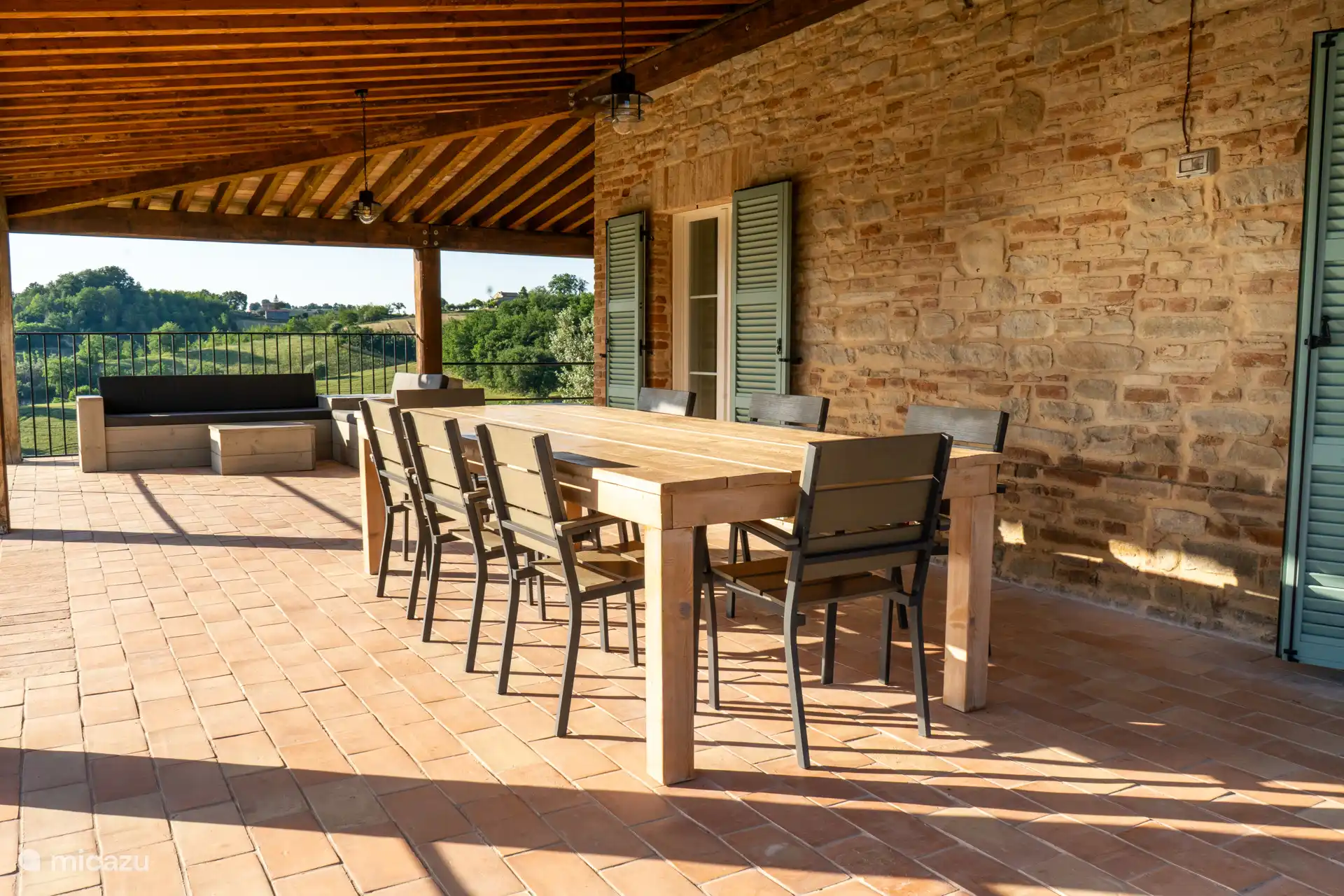 Op het terras, een grote houten eettafel en zithoek met bbq plancha grill.