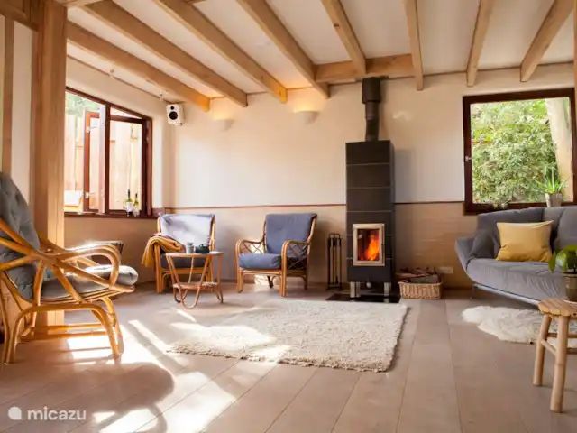 Location de Vacances Pays-Bas, Hollande du Nord, Schoorl, maison de vacances - Ecole Ecolodge de Parel Le salon avec poêle de masse. Après 1,5 heure de cuisson, le poêle dégage de la chaleur pendant environ 13 heures. Sur la droite se trouve un canapé-lit. Il y a aussi un pouf pour que les enfants puissent s'allonger devant le poêle.