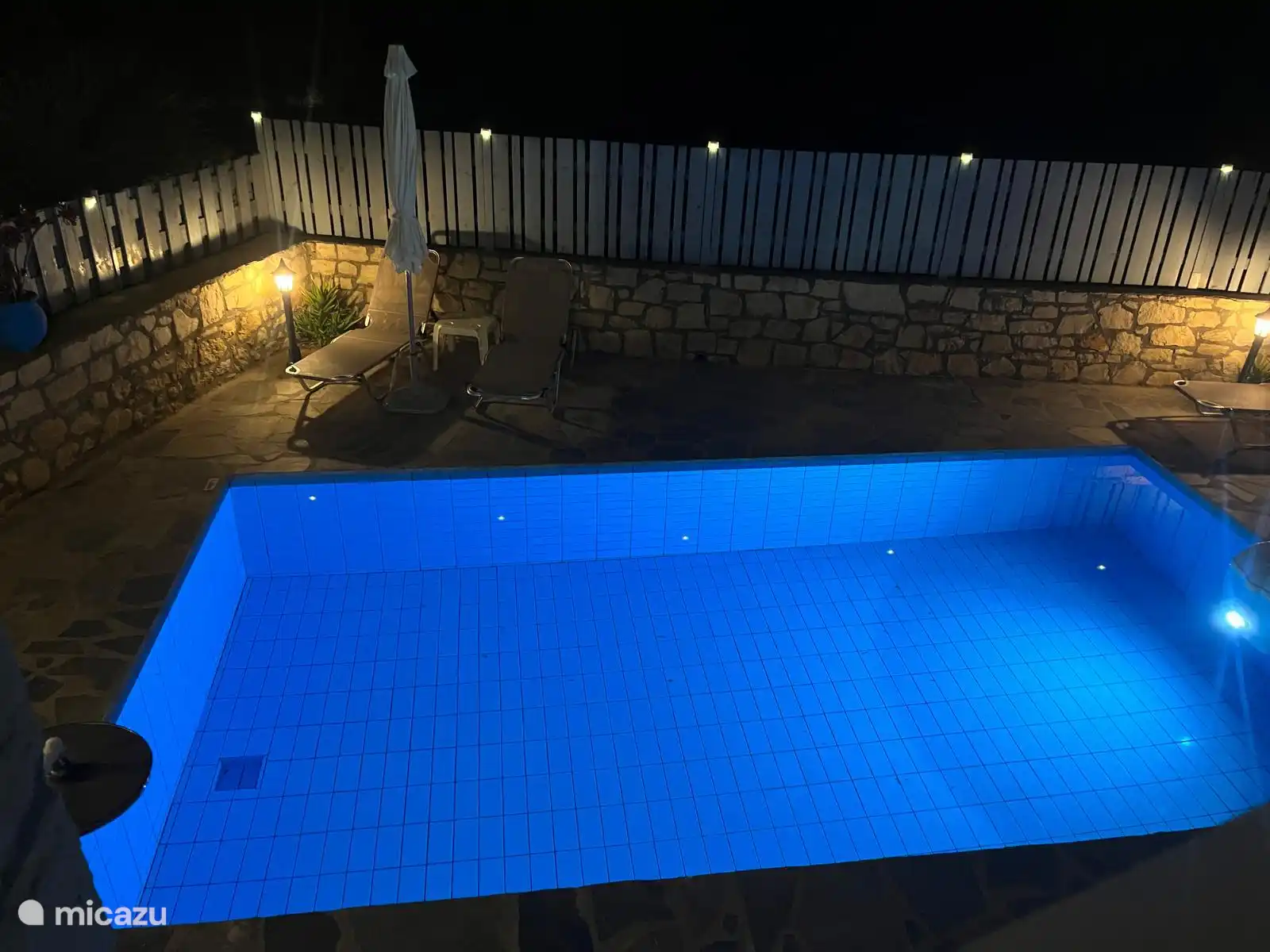 Zicht op verlicht zwembad vanaf het terras; oftewel pool by night.