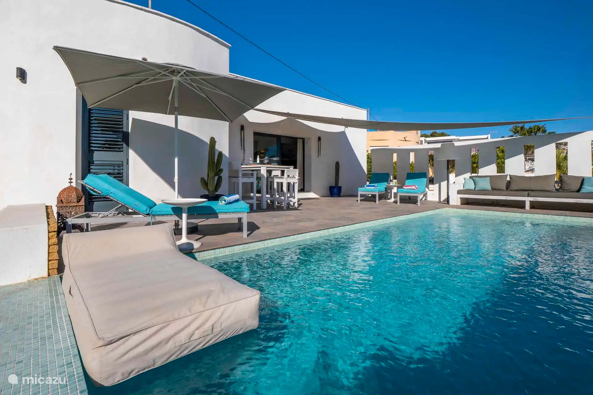 Vista panorámica de la terraza desde la piscina, tumbado en el gran sofá, desayunando o tomando algo en la mesa alta de la barra y relajándose en las tumbonas.