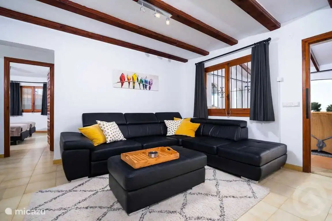 Le salon avec un grand canapé en cuir avec chaise longue. Accès direct à la véranda et hall avec chambres.