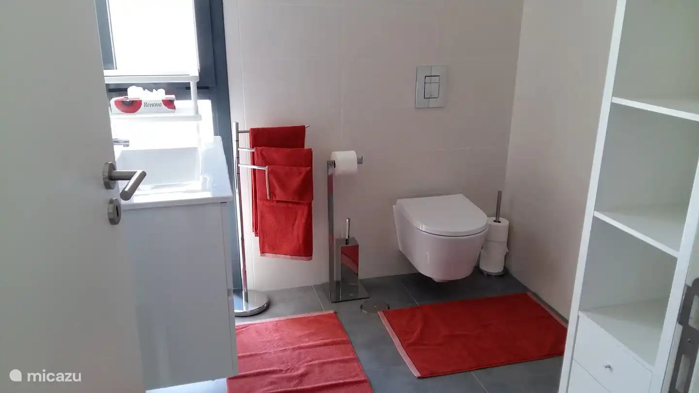 Das Badezimmer im Erdgeschoss mit Dusche, Waschbecken und WC und angrenzend an das orange Schlafzimmer, mit den passenden Badetextilien. 