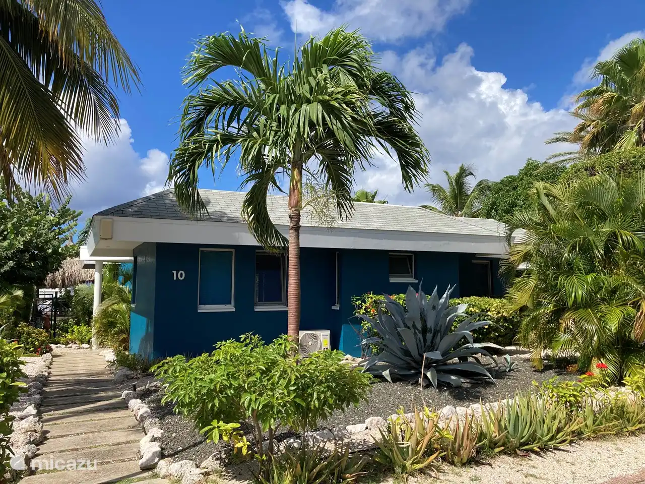 Façade de la maison avec l'allée pour la voiture à droite et l'allée vers le jardin à gauche