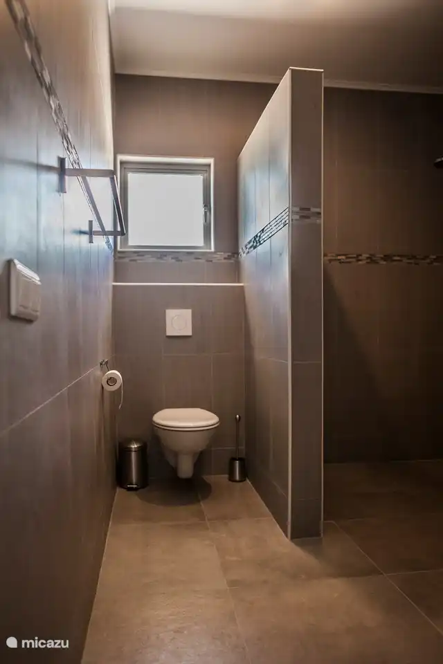 El baño junto al dormitorio principal con inodoro, ducha a ras de suelo y lavabo doble.